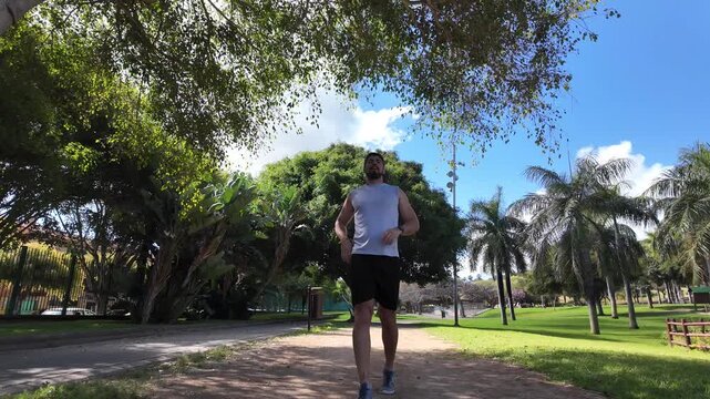 Young man stopping to rest after running in park in slow motion