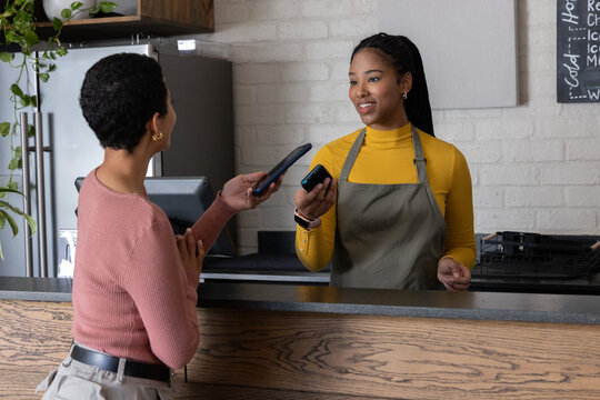 Female server wearing gray apron, patron showing phones, tapping reader at cafe counter, copy space