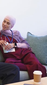 Vertical video: Starting chat, medical staff in scrubs talking on couch during break with coffee