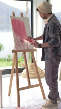 Vertical video: Dipping brush, Indian artist painting pink drips to fill canvas at home, copy space
