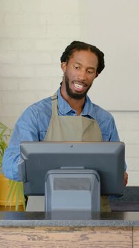 Vertical video: Customer handing device, cashier in beige apron tapping POS at counter, charging