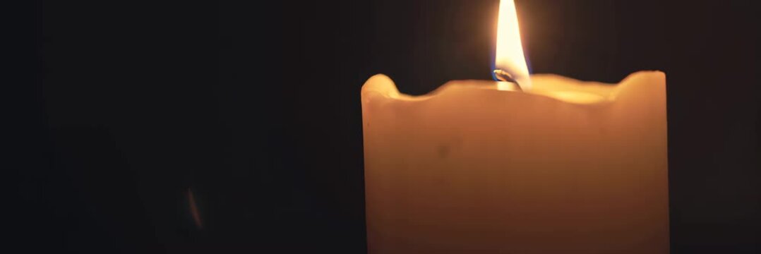 Burning candle flame on dark background with copy space, warm light banner video background for website header and landing page.