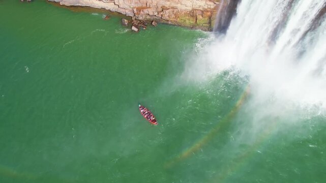 Top-down drone view of Chitrakote Waterfall with boat and rainbow in green water.
