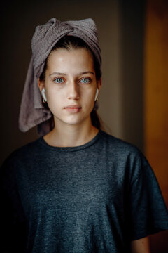 Natural portrait of a teen girl after a shower, with a towel on her head and earphones. Home lifestyle image for themes of morning routine, self care, natural skin and teenage everyday life.