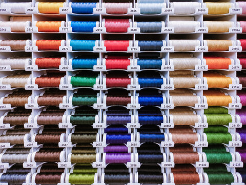 Horizontal close-up photo with a dense display of colorful thread spools. Suitable for sewing, textile industry, tailoring, atelier and craft supply themes.