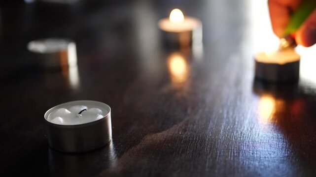 Close up motion of igniting small tea light candles with a green lighter, creating a warm and intimate atmosphere in soft focus background