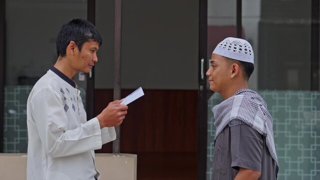 Muslim man in white koko shirt receiving envelope or donation from religious teacher