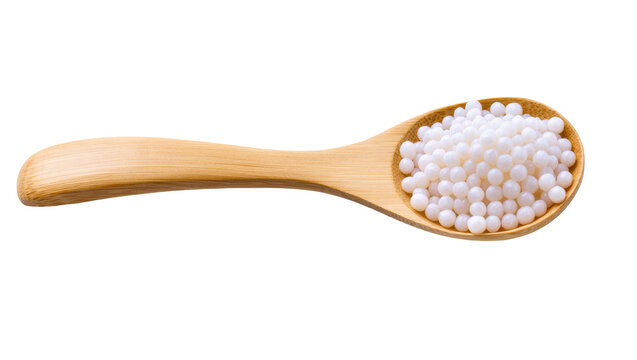 Isolated wooden spoon filled with numerous small white round homeopathic sugar pills.
