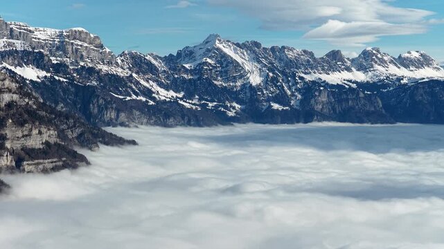 Snow-covered mountain range rising above dense valley cloud inversion near Walensee, Switzerland