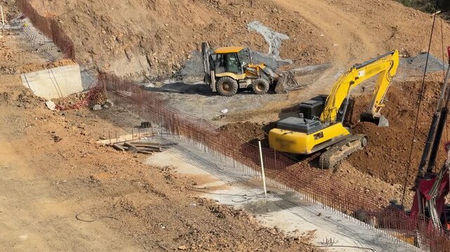 High-angle view of yellow excavator and backhoe loader machines performing earth excavation and foundation preparation at a large construction site. Urban development projects.