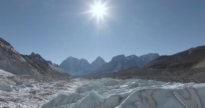 Khumbu Glacier and the Khumbu Icefall with towering ice formations and melt-water sources surrounded by rugged Himalayan mountains under a clear midday sky in Nepal.