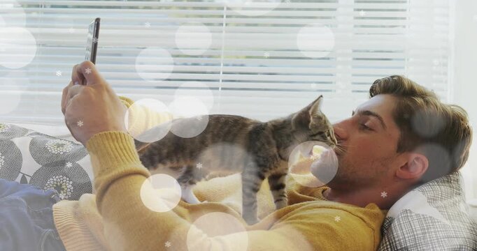 Man lying on couch holding phone while kitten climbing torso, sniffing and nuzzling, pet care bokeh