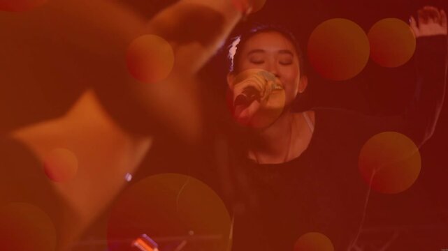 Woman singer singing into wired mic under bokeh lights, music crowd arm reaching, leaning, engaging