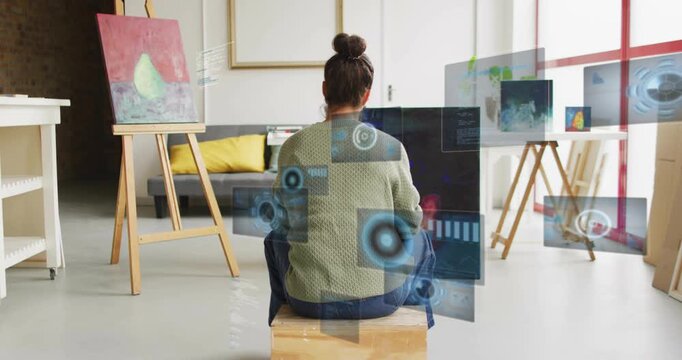 Artist sitting on box facing canvas in art studio camera shifting showing AR panels testing layout