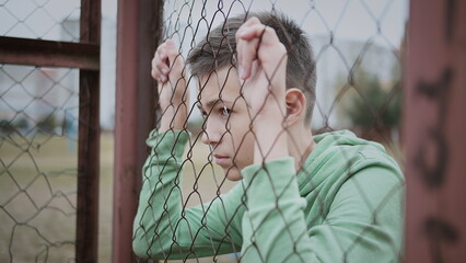 cinematic refugee sad boy stands alone head bowed near the fence, frustrated boy dropped eyes, have fun and enjoy © vla