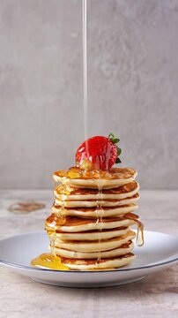 honey pouring over a stack of pancakes with strawberries