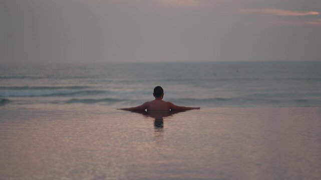 Luxury infinity pool at sunset in Bali with man relaxing and ocean view, tropical travel destination, serene lifestyle scene