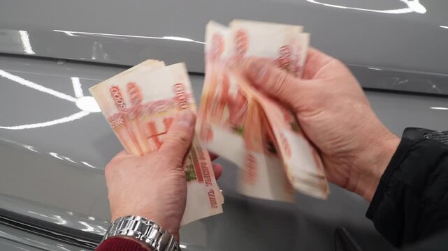 A close-up of a man's hands counts a bundle of bills for five thousand Russian rubles. Man counts red paper 5000 rubles bills. Russian cash money in male hand. A man holds a wad of money in his hands.