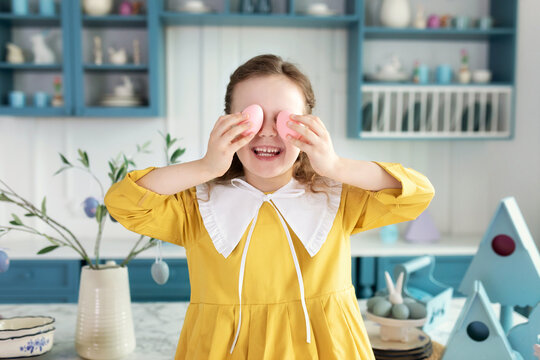 Closeup Portrait of funny cute kid girl covering eyes with Easter eggs. Cheerful beautiful smiling little girl holding an easter eggs in her hands, closes eyes, kid celebrate easter.