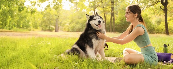 Sporty young woman with cute Husky dog sitting on grass in park © Pixel-Shot