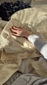 Morning sunlight casting soft shadows over a rumpled bed as a relaxed hand rests on the duvet, intimate moment symbolizing waking up slowly after a restful night at home.