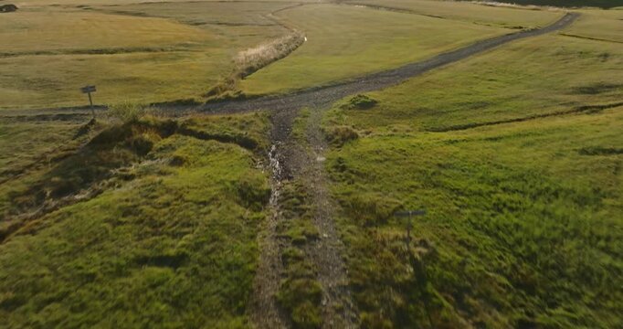 Breathtaking drone footage captures rolling green hills and golden grasslands in rural Iceland during golden hour. A winding stream cuts through the pastoral landscape as dramatic sunlight
