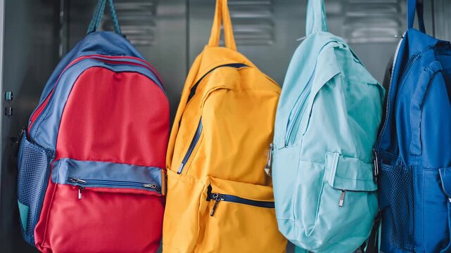 Colorful backpacks hanging on hooks in a metal locker. School supplies in an empty college hallway, representing education and student life