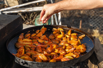 Seasoned roasted potatoes in outdoor pan. Close-up of crispy potato wedges being seasoned in a...