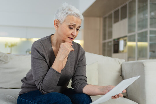 Sad tired ill sick lonely disappointed older senior woman reading bad news at home alone. Unhappy mature grandmother experiencing grief relative death. Stressed elder lady with paper document bill