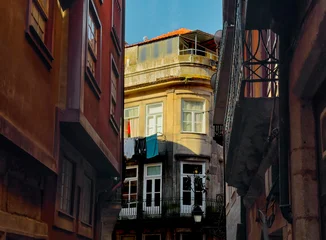 Fotobehang Smal steegje Narrow alley with warm colored buildings and sunlight in Guimaraes. Perspective leads toward bright facade at end of street composition. Travel concept showing atmospheric European city  © valiantsin
