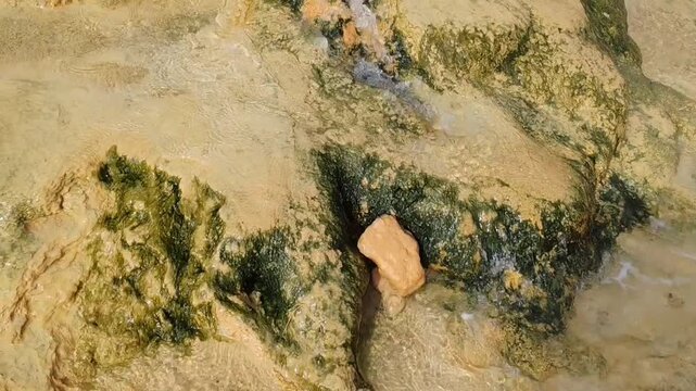  Hot thermal springs flowing into the sea in Loutra Edipsou, Evia, Greece. Natural sulfur water waterfall on a rocky beach with steam and mineral deposits