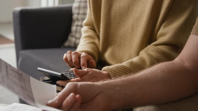 Close-up view of hands of unrecognisable senior couple calculating utility costs while analyzing their budget