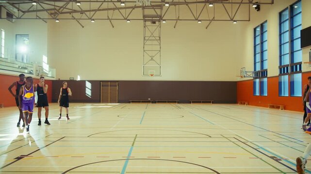 An athletic young man actively plays basketball indoors. He skillfully dribbles, jumps, and shoots the ball, scoring a perfect hoop. The scene captures dynamic sports action and youth.