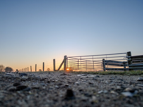 Open metal farm gate on gravel road at sunrise in rural countryside