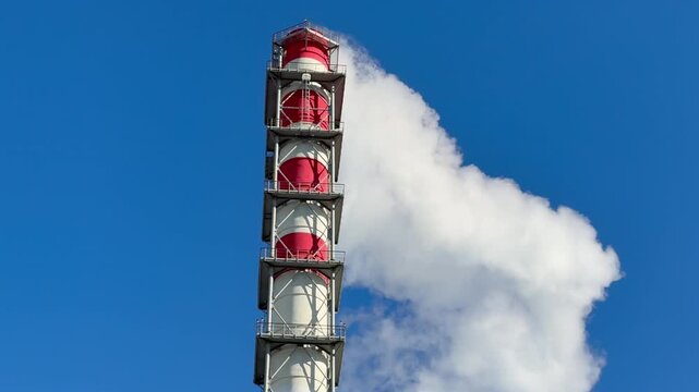 CHP emissions. Smoking chimney releasing smoke against a blue sky. Smoke from factory pipe of heat station in the city. Air pollution. Nuclear power plant cooling. CO2, greenhouse gases emissions.