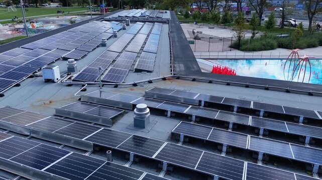 Drone aerial shot: solar panels cover roof of public outdoor swimming pool in Halifax. Renewable energy production in urban setting, Nova Scotia Canada, bright daylight view 4K.