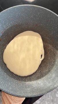 Fresh liquid pancake dough pouring from a ladle onto a hot frying pan.
