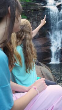 Happy mother and daughter talking by a forest waterfall in Norway. Bright northern daylight, authentic family bonding and sustainable travel concept.
