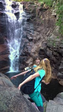 Mother and daughter admiring a misty forest waterfall in Norway from behind. Authentic back view, sustainable travel and mental health wellness through nature immersion.