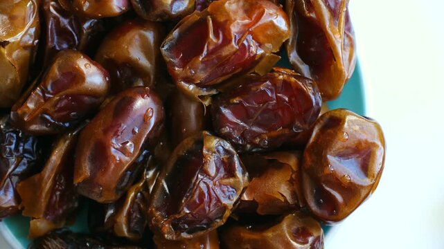 Delicious dried date fruits in turquoise bowl rotating slowly on white background, healthy sweet snack for vegan diet, important food during holy month of ramadan. Healthy fresh dates rotating in bowl