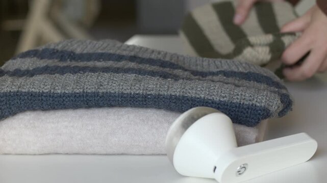 Hand smoothing striped knit sweater after fabric shaver lint removal as final step of clothing care. Garment finishing suits sustainable fashion, conscious consumption and textile maintenance concept 