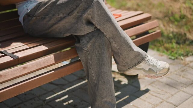 park bench legs crossed elderly white retiree sitting quietly, soft sunlight on pavement, textured trousers and worn sneakers, slow breathing, peaceful solitude and gentle shadow under wooden slats,
