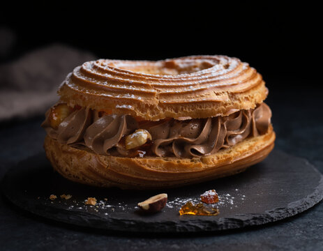 Paris-Brest coup&eacute; r&eacute;v&eacute;lant cr&egrave;me pralin&eacute;e et noisettes caram&eacute;lis&eacute;es, &eacute;clairage lat&eacute;ral dramatique sur fond sombre