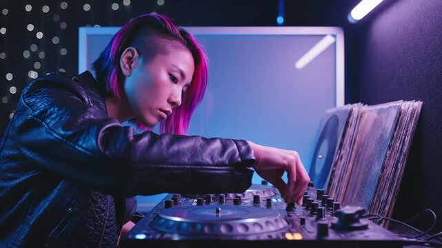 Female DJ mixes music on turntable in neon studio light. Woman DJ adjusts mixer controller with vinyl records. DJ performs mixing on turntable. Female artist works with music controller in studio.