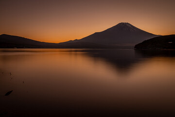 Obraz premium 夕暮れの山中湖に映る富士山と黄金色に染まる静かな水面