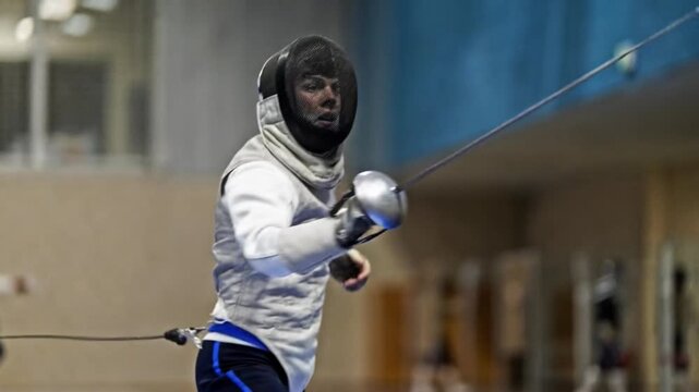 Focused fencing fencer sword sport athlete action competition in indoor arena wearing protective mask and padded uniform during intense duel and training motion blur concentration