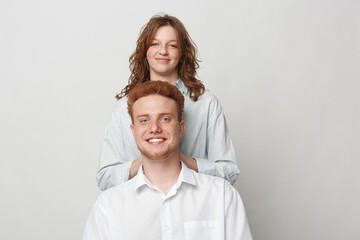 Fototapeta premium Smiling young man and woman with casual clothes pose together on light background. Friendly couple with natural expressions shows positive mood and relaxed lifestyle concept.