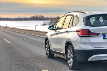 Fototapeta premium Modern station wagon driving on winter highway at sunset through snowy countryside. Car travel.