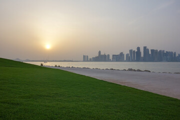 Fototapeta premium Doha, Qatar - sunset over Doha skyline with green park and waterfront along the bay.