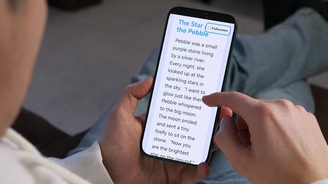 A person uses a mobile e-learning app to read an interactive story. Featuring a Read To Me function, this shot is perfect for educational technology, digital literacy, and children's app marketing